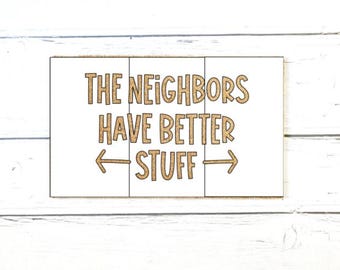 May include: A rectangular doormat with a white surface divided into three vertical sections. The text "THE NEIGHBORS HAVE BETTER STUFF" is printed in brown, along with a left-pointing arrow and a right-pointing arrow on the bottom line.