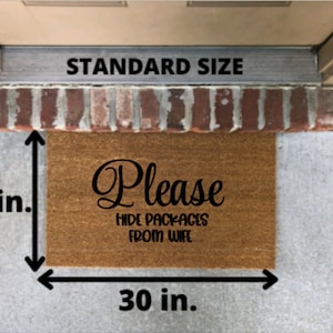 May include: A rectangular brown coir doormat featuring the black text Please HIDE PACKAGES FROM WIFE. The mat is labeled as standard size with visible measurement arrows indicating a width of 30 inches and a height of 18 inches on the mat surface.