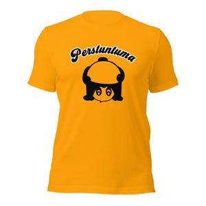 May include: Mustard yellow t-shirt with a black graphic of a cartoon character and the word "Perstuntuma" in a script font. The graphic features a round head and a smiling face.