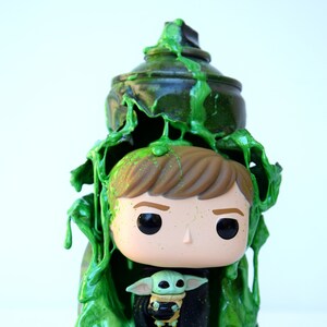 Peut inclure: Une figurine en vinyle vert et noir d'un personnage de la franchise Star Wars. La figurine tient une plus petite figurine en vinyle verte d'un personnage de la franchise Star Wars. Les figurines sont recouvertes de slime vert.