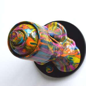 May include: A colorful spray paint can sculpture with a black base. The can is dripping with paint, creating a dynamic and abstract design.