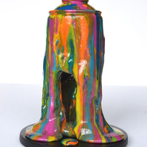 May include: A colorful, abstract sculpture of a spray paint can with dripping paint. The sculpture is made of resin and is painted in a variety of colors, including pink, orange, yellow, green, and blue. The sculpture is sitting on a black base.