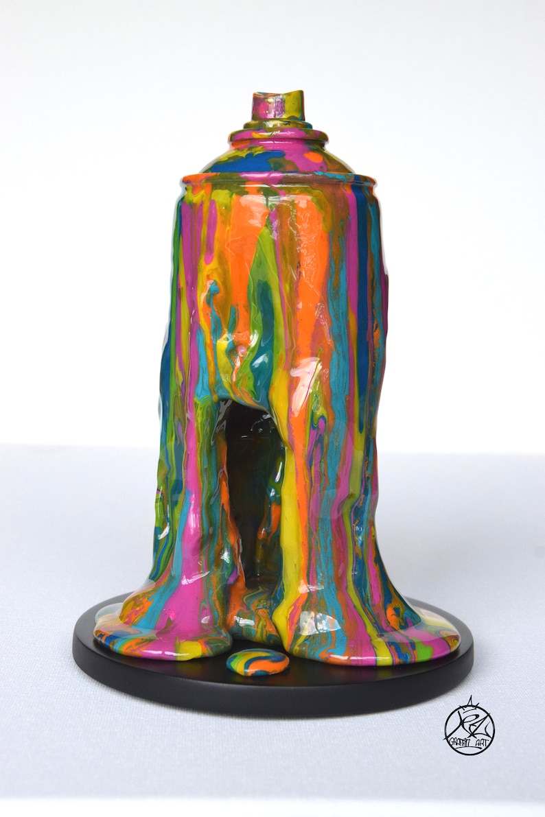 May include: A colorful, abstract sculpture of a spray paint can with dripping paint. The sculpture is made of resin and is painted in a variety of colors, including pink, orange, yellow, green, and blue. The sculpture is sitting on a black base.
