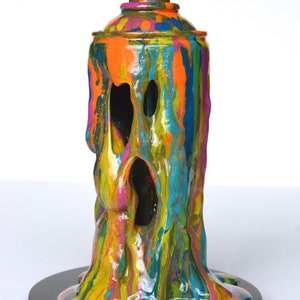 May include: A colorful, abstract sculpture of a spray paint can, dripping with paint. The sculpture is made of resin and is painted in a variety of colors, including orange, yellow, green, blue, and pink. The sculpture is mounted on a black base.