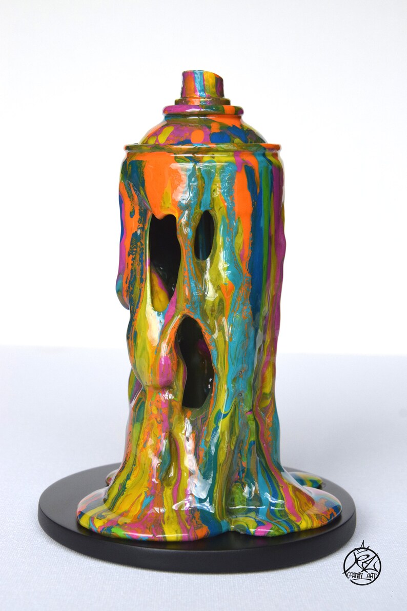 May include: A colorful, abstract sculpture of a spray paint can, dripping with paint. The sculpture is made of resin and is painted in a variety of colors, including orange, yellow, green, blue, and pink. The sculpture is mounted on a black base.