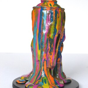 May include: A colorful, abstract sculpture of a spray paint can with dripping paint. The can is made of resin and is painted in a variety of bright colors, including pink, blue, green, yellow, and orange. The paint is dripping down the sides of the can, creating a dynamic and abstract effect.