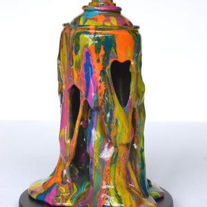 May include: A colorful, abstract sculpture of a spray paint can with dripping paint. The sculpture is made of resin and is painted in a variety of colors, including blue, green, yellow, orange, and pink. The sculpture is sitting on a black base.