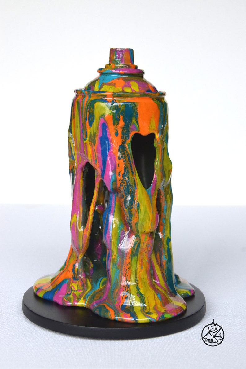 May include: A colorful, abstract sculpture of a spray paint can with dripping paint. The sculpture is made of resin and is painted in a variety of colors, including blue, green, yellow, orange, and pink. The sculpture is sitting on a black base.