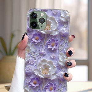 May include: A clear phone case with a 3D floral design. The flowers are white and purple with a textured, embossed look. The case is designed for an iPhone.
