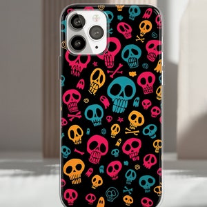 Puede incluir: Una funda de tel&eacute;fono negra con un patr&oacute;n repetido de calaveras de dibujos animados coloridas en rosa, amarillo, azul y naranja. La funda tiene un borde transparente y cubre la parte trasera del tel&eacute;fono.