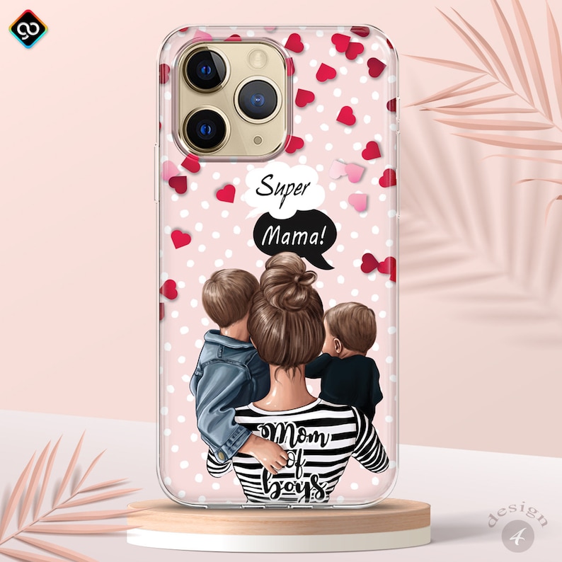 May include: A clear phone case with a pink background and white polka dots. The case features a cartoon illustration of a woman with two children, with the text "Super Mama!" in a speech bubble. The woman is wearing a striped shirt with the text "Mom of Boys" on it. The case is decorated with red and pink hearts.