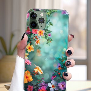 May include: Clear phone case with a floral design. The case features a variety of colorful flowers, including pink, purple, yellow, and orange, on a green and blue background.