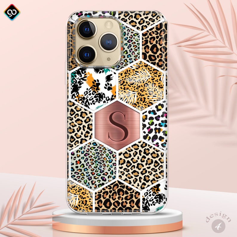 May include: A clear phone case with a geometric pattern of different leopard prints in shades of brown, black, white, pink, and blue. The case has a rose gold hexagon with the letter "S" in the center.