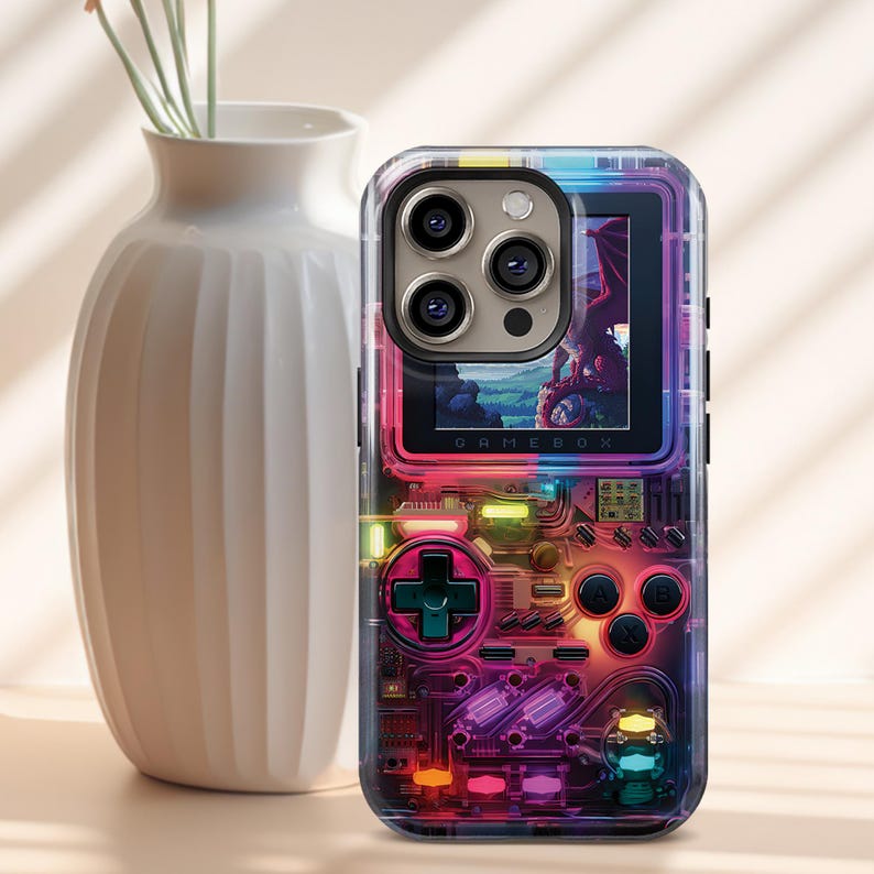 May include: Clear phone case with a colorful design resembling a retro handheld game console. The case features a screen displaying a dragon image, with the word "GAMEBOX" visible. The case has a D-pad and buttons.