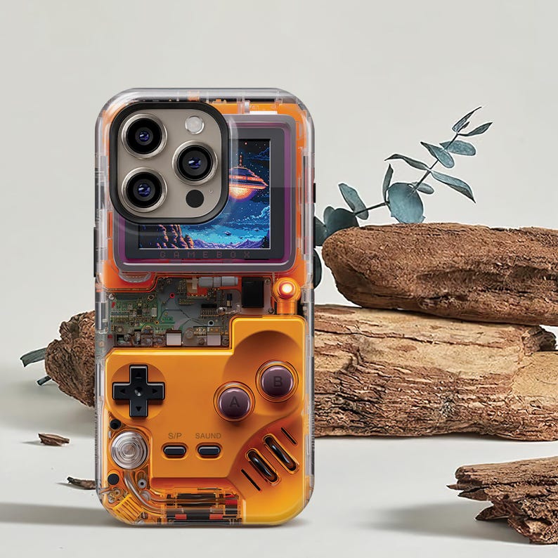May include: Clear phone case with an orange retro game controller design. The case features a screen displaying a colorful space scene. The design includes a directional pad, buttons, and circuit board details, offering a nostalgic aesthetic.