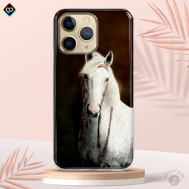 Op de afbeelding: Een transparante telefoonhoes met een wit paard met een bruin leren hoofdstel op een donkerbruine achtergrond.
