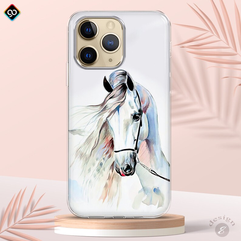 Op de afbeelding: Een transparante telefoonhoes met een aquarel schilderij van een wit paardenhoofd. Het paard heeft een roze neus en een zwart halster. De hoes is ontworpen voor een iPhone.