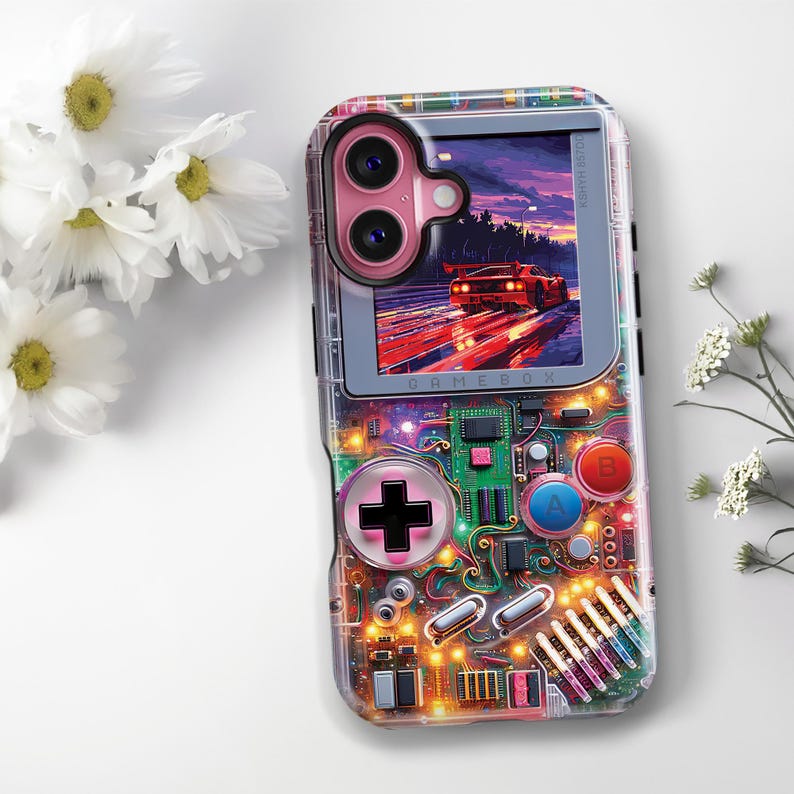 May include: Clear phone case with a colorful design resembling a retro handheld game console. The case features a pink camera cutout and a screen displaying a car racing scene. The design includes buttons, circuits, and the word "GAMEBOX".