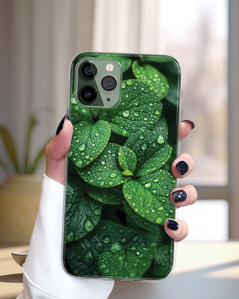 May include: A clear phone case with a green leafy design. The leaves have water droplets on them.