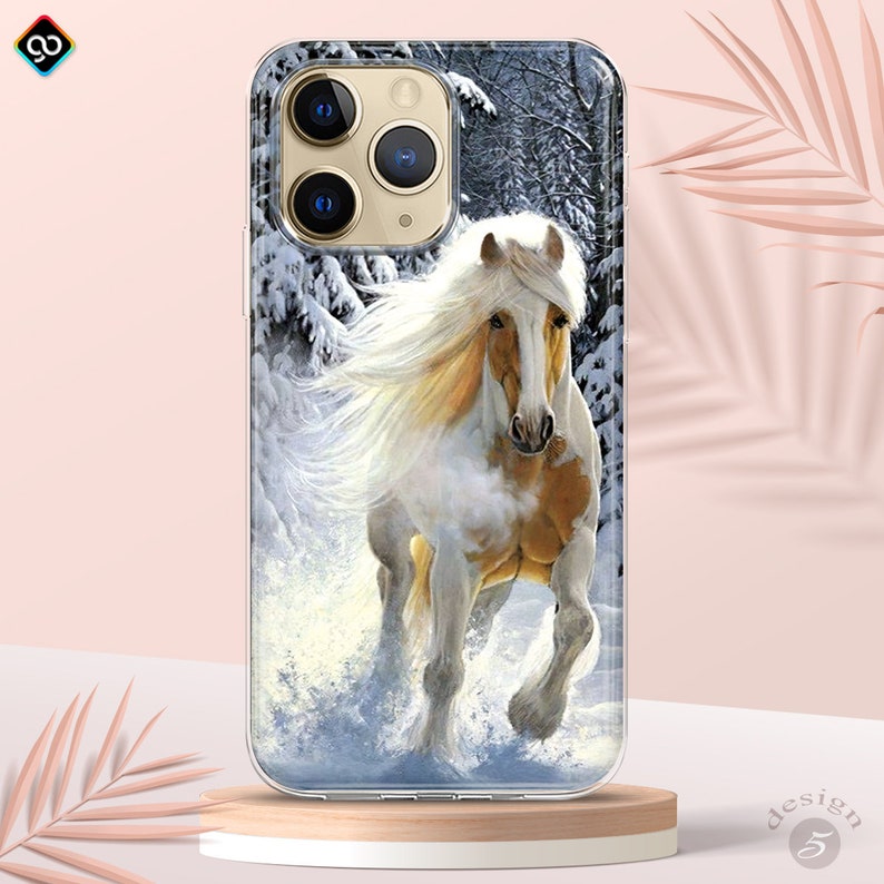 Op de afbeelding: Een wit en bruin paard met een lange, stromende manen rent door een besneeuwd bos. Het paard is scherp in beeld en de achtergrond is wazig. De afbeelding is op een transparante telefoonhoes.