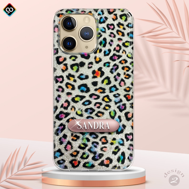 May include: A clear phone case with a glittery leopard print design in rainbow colors. The case has a rose gold nameplate with the name "SANDRA" on it.