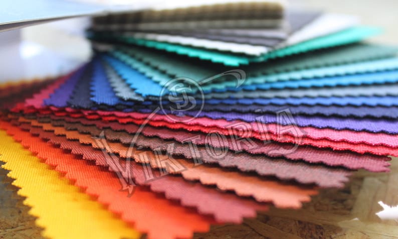 May include: A fan of fabric swatches in various colors, including yellow, orange, red, purple, blue, and green. The fabric samples are arranged in a layered, fanned-out display, showcasing a range of hues and textures. The edges of the fabric are cut in a wavy pattern.