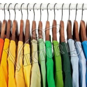 May include: A row of colorful t-shirts hanging on wooden hangers. The shirts are arranged in a rainbow spectrum, from red to purple. The hangers are suspended from a white rod with black hooks, creating a visually appealing display.