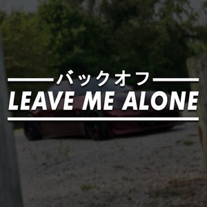 Può includere: Un'auto rossa con la scritta "LEAVE ME ALONE" in lettere bianche sul retro. Il testo "バックオフ" è scritto in giapponese sopra la scritta "LEAVE ME ALONE".