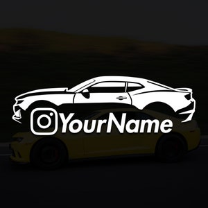 Puede incluir: Silueta blanca de un coche con el logotipo de Instagram y el texto "YourName" debajo. El coche está parcialmente oculto por un coche amarillo.