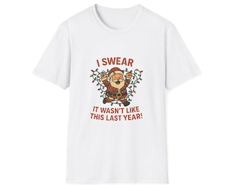 May include: White t-shirt with a cartoon Santa Claus design, entangled in Christmas lights. The text "I SWEAR IT WASN'T LIKE THIS LAST YEAR!" is printed above and below the Santa illustration. A festive holiday-themed tee.