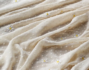 May include: White sheer fabric with a dotted texture and embroidered white daisies. The fabric is folded and draped.