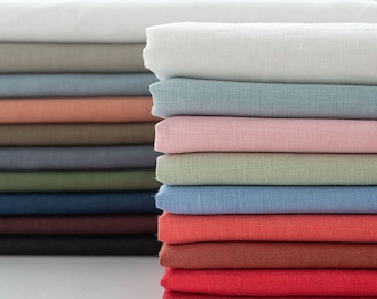 May include: A stack of 14 different colored linen fabrics. The fabrics are folded and stacked on top of each other. The fabrics are all different shades of blue, green, red, orange, pink, and brown.