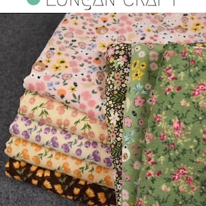 May include: A stack of fabric featuring various floral patterns in pink, yellow, green, and brown. The fabric is folded neatly and has a soft, textured feel.