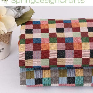 May include: Close-up of a stack of woven fabric with a colorful checkerboard pattern. The squares are in shades of red, orange, yellow, green, blue, and black. The text "SpringdesignCrafts" is visible in the background.