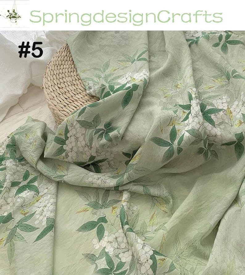 Peut inclure: Tissu vert clair avec un motif floral de fleurs blanches et de feuilles vertes. Le tissu est drap&eacute; sur un panier en osier. Le texte "SpringdesignCrafts" et "#5" sont visibles.