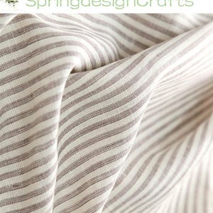 Op de afbeelding: Een stof met een patroon van dunne, verticale bruine en gebroken witte strepen. Het materiaal is gedrapeerd om plooien en textuur te tonen, met de tekst SpringdesignCrafts zichtbaar in de linkerbovenhoek van het afbeeldingskader.