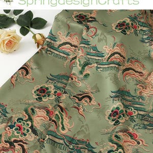 May include: A sage green fabric featuring an intricate embroidered pattern of traditional pagodas, stylized floral motifs, and swirling cloud designs in shades of dark green, deep red, and soft peach, accented by a single cream-colored rose.