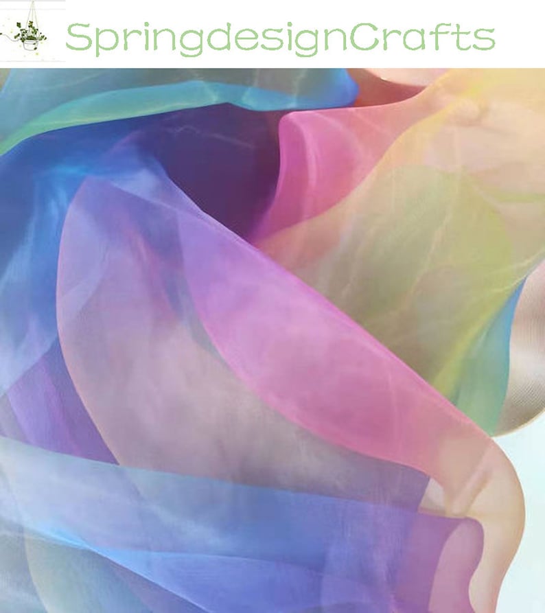 May include: A close-up of flowing, sheer fabric in a rainbow of colors, including pink, blue, yellow, and purple. The fabric is layered and creates a soft, ethereal effect. The text "SpringdesignCrafts" is in the upper left corner.
