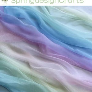 May include: Soft, flowing fabric in a gradient of colors, including blue, purple, pink, and green. The fabric is arranged in gentle waves, creating a sense of movement. The text "SpringdesignCrafts" is visible in the upper left corner.