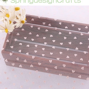 May include: White sheer fabric with a pink heart pattern. The fabric is draped over a wooden crate.