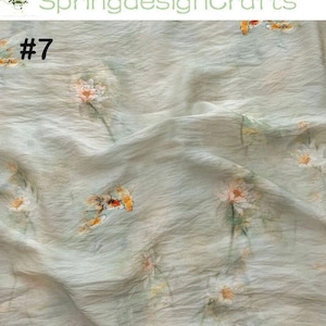 Peut inclure: Tissu bleu clair avec un motif floral. Le tissu a une texture froiss&eacute;e et pr&eacute;sente des fleurs &eacute;parses dans les tons de blanc, d'orange et de jaune. Le num&eacute;ro "#7" est imprim&eacute; en haut &agrave; gauche, et le texte "SpringdesignCrafts" est imprim&eacute; en haut.