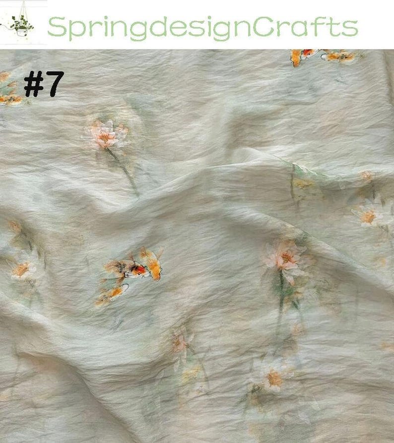 Peut inclure: Tissu bleu clair avec un motif floral. Le tissu a une texture froiss&eacute;e et pr&eacute;sente des fleurs &eacute;parses dans les tons de blanc, d'orange et de jaune. Le num&eacute;ro "#7" est imprim&eacute; en haut &agrave; gauche, et le texte "SpringdesignCrafts" est imprim&eacute; en haut.