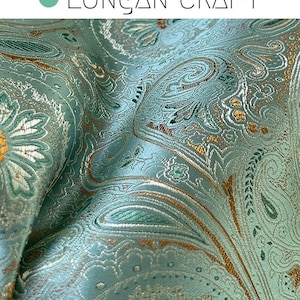 May include: Close-up of a teal fabric with a paisley pattern in gold and green. The fabric has a subtle sheen and a textured surface.