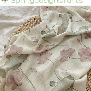 Peut inclure: Tissu blanc cass&eacute; avec un motif floral d&eacute;licat de fleurs de lotus roses et de feuilles vertes. Le tissu est drap&eacute; sur un panier en osier, avec le texte "SpringdesignCrafts" en vert.