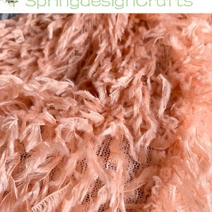 May include: Close-up of a peach-colored fabric with a fuzzy texture. The fabric has a delicate, net-like base with long, soft strands of fabric extending from it.