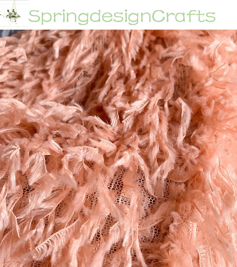 May include: Close-up of a peach-colored fabric with a fuzzy texture. The fabric has a delicate, net-like base with long, soft strands of fabric extending from it.