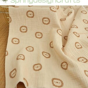 May include: Cream-colored muslin fabric with a repeating pattern of brown lion faces. The fabric is soft and textured, with a crinkled appearance. The text "SpringdesignCrafts" is visible in the upper left corner.