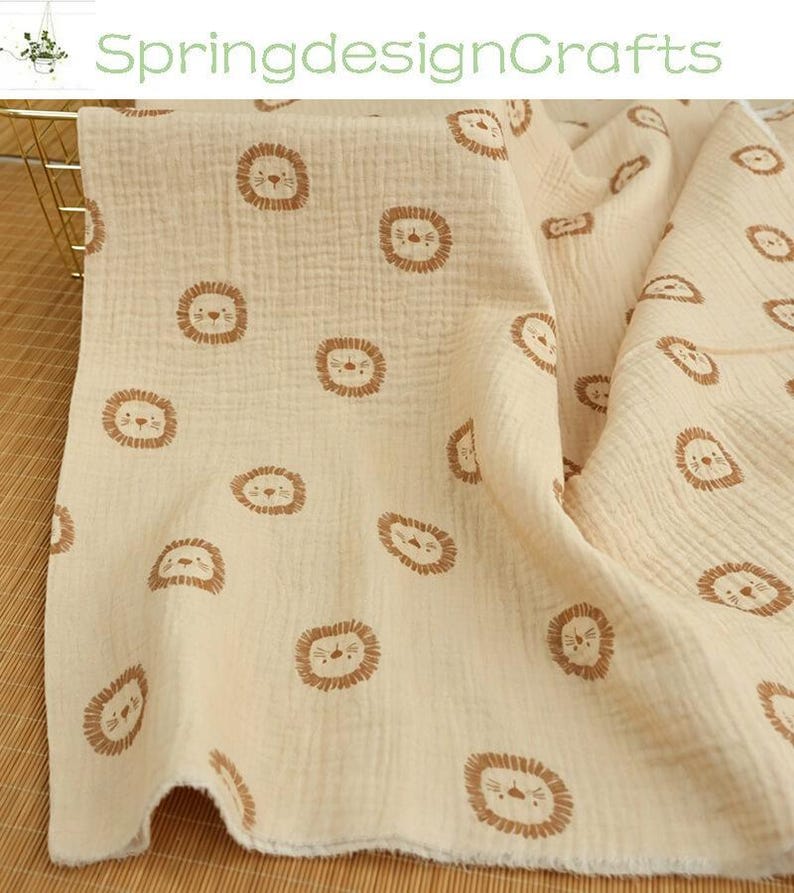 May include: Cream-colored muslin fabric with a repeating pattern of brown lion faces. The fabric is soft and textured, with a crinkled appearance. The text "SpringdesignCrafts" is visible in the upper left corner.