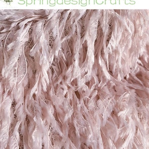 May include: Close-up of a soft, pink feather trim fabric. The fabric has a delicate, fluffy texture and is perfect for adding a touch of elegance to any project.