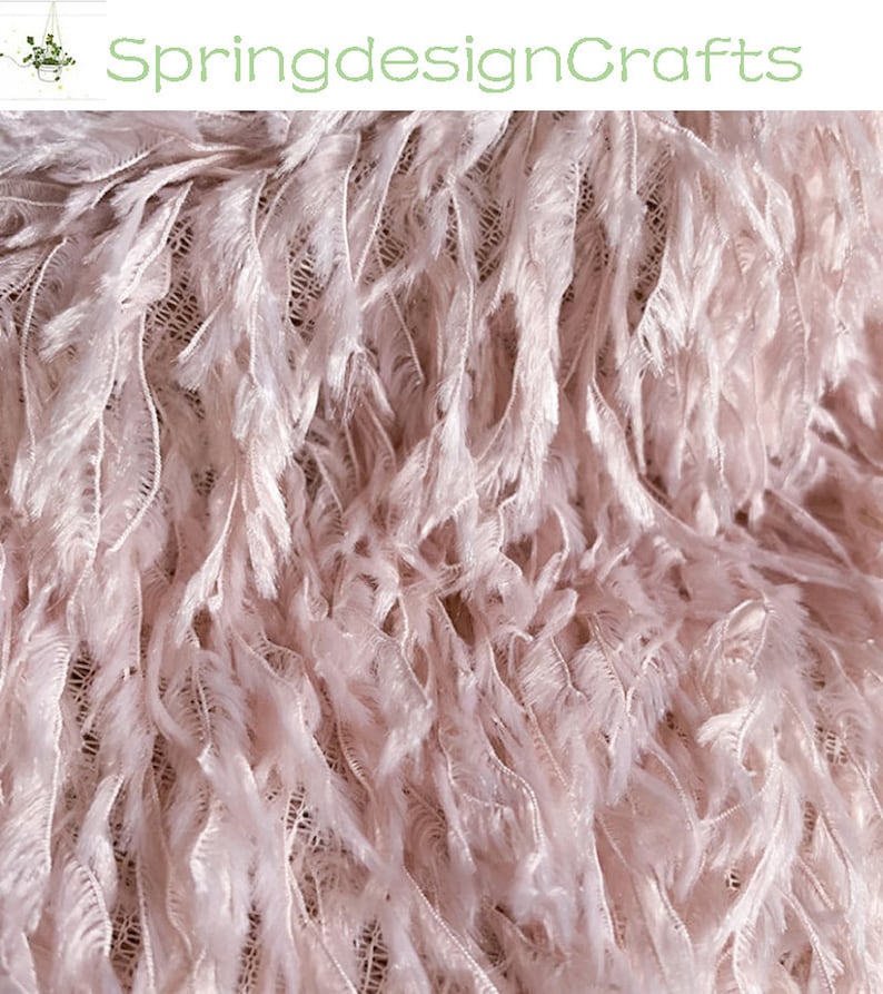 May include: Close-up of a soft, pink feather trim fabric. The fabric has a delicate, fluffy texture and is perfect for adding a touch of elegance to any project.
